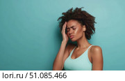 A young African woman with curly hair holds her head in distress against a blue background. She appears to be experiencing discomfort or stress. Стоковое AI-видео, аниматор Nart / Фотобанк Лори
