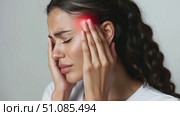 A young Middle-Eastern woman with curly hair holds her head in pain, showing signs of a headache. She has a distressed expression and is wearing a white shirt. Стоковое AI-видео, аниматор Nart / Фотобанк Лори
