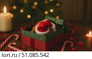 A calico cat's tail is visible from a decorated gift box. The scene includes candles, candy canes, and a Christmas tree in the background. Стоковое AI-видео, аниматор Nart / Фотобанк Лори