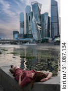 Young woman in a burgundy dress relaxing on a stone embankment, lying with her head back and hand resting on her forehead near the water. Редакционное фото, фотограф Софья Соломонова / Фотобанк Лори