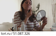 Attractive brunette mid adult woman putting on makeup looking in the mirror. Beautiful lady caring her face. 40 years old female applied cosmetics. Natural beauty and aging concept. Skin care, make-up. Стоковое видео, видеограф Марина Демидюк / Фотобанк Лори