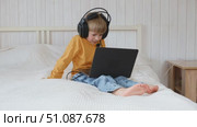 Little smiling 6 years old boy using a laptop with headphones. Child having video call with friends, granny at home in bed. Kid looking at display and waving hand. Childhood leisure activity concept. Стоковое видео, видеограф Марина Демидюк / Фотобанк Лори