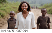 Volunteer woman teacher walks with poor African children along a dirt road in rural Africa. Black African children from disadvantaged families study in school, read books, receive primary education, volunteer service. Стоковое AI-изображение, AI-художник ALLA YURTAYEVA / Фотобанк Лори