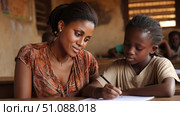 An African teacher assisting a student with math homework in a warm, welcoming classroom setting. Black African children from disadvantaged families study in school, read books, receive primary education, volunteer service. Стоковое AI-изображение, AI-художник ALLA YURTAYEVA / Фотобанк Лори