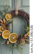 A festive Christmas wreath made of evergreen branches, decorated with dried orange slices, pine cones, and wooden accents, hanging on a blue door. Стоковое AI-видео, аниматор Nart / Фотобанк Лори