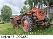 Vintage red old tractor t16 parked in a lush green field near a rustic farmhouse on a cloudy day in the countryside. Стоковое фото, фотограф Владимир Разгуляев / Фотобанк Лори