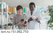 Woman in pharmacy scans QR code on antitussive syrup. African man pharmacist in background. Стоковое видео, видеограф Яков Филимонов / Фотобанк Лори