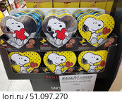 A store display with gift sets of chocolate pralines in heart-shaped tins. The packages feature the popular comic book character Snoopy: on some lids he holds a red heart, on others - a bouquet of red flowers. The design is bright and festive: metal boxes with a silver sheen and yellow boxes with polka dots create a joyful mood. Such a product is ideal for gifts for Valentine's Day, birthdays or other festive events. (2019 год). Редакционное фото, фотограф Анна Кривицкая / Фотобанк Лори