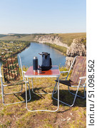 Summer travels and picnic on high bank of beautiful Belaya river. Tourist table, folding chairs, thermal bag with snacks and thermos on background of riverside on sunny August day. Acive recreation. Стоковое фото, фотограф Виктория Катьянова / Фотобанк Лори
