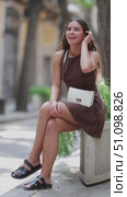 Young european girl in dress sitting concrete flower bed with plants, relaxing and posing on shaded street in Barcelona. Стоковое видео, видеограф Яков Филимонов / Фотобанк Лори