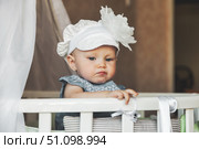 Little Dreamer in Fancy Bonnet Stands in White Crib Contemplating Existence. Стоковое фото, фотограф Aleksandr Golubev / Фотобанк Лори