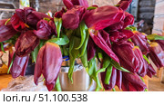 A bouquet of burgundy tulips with rich green leaves. The flowers are tightly packed, their buds have not yet fully opened, which creates a feeling of freshness and natural liveliness. The bouquet is placed in a metal pot, which gives the composition an unusual and slightly rustic character. The background is blurred, but wooden interior elements and household details are guessed, emphasizing the atmosphere of coziness and simplicity. The photo conveys the beauty of natural forms and the contrast of the deep burgundy shade of the petals with the bright green foliage. Стоковое фото, фотограф Анна Кривицкая / Фотобанк Лори