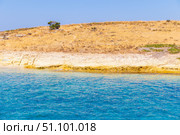 A tranquil scene featuring a crystal-clear turquoise sea gently lapping against a dry, rocky coastline under a cloudless blue sky. This peaceful landscape evokes the essence of summer and natural beauty, possibly located on a Mediterranean or Aegean island. The arid golden hill contrasts beautifully with the vibrant water, making this image ideal for travel, vacation, nature, or seascape themes. Стоковое фото, фотограф Анастасия Мерчик / Фотобанк Лори