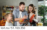 Friendly young parents with preteen son making purchases in local grocery store, using smartphone to scan barcodes on bottles of juices. Modern shopping and family teamwork concept. Стоковое видео, видеограф Яков Филимонов / Фотобанк Лори