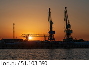 Port cranes for cargo transshipment on the mooring line of the Astrakhan port on the right bank of the Volga River against the background of the setting sun, Astrakhan, Russia. Стоковое фото, фотограф Ula Ulachka / Фотобанк Лори