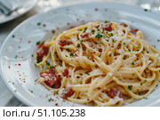 Delicious linguine pasta with bacon, cheese, parsley and spices on elegant white plate. Стоковое AI-изображение, AI-художник Иван Рябоконь / Фотобанк Лори