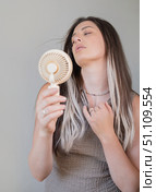 Tired young woman enjoying cool air with a lightweight portable fan outdoors on a warm sunny summer day. Стоковое фото, фотограф Svetlana Golovco / Фотобанк Лори
