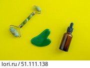 Bottle for cosmetics and jade massagers on a yellow background. Beauty saloon. Background with copy space. Стоковое фото, фотограф Юлия Николаева / Фотобанк Лори