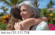 Senior woman warmly embracing younger woman in lush garden setting, expressing love, connection, and emotional closeness in a joyful outdoor moment. Стоковое AI-изображение, AI-художник Катерина Бондарец / Фотобанк Лори