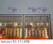 Refrigerated display case in a supermarket with Valio brand products. Yogurts in plastic cups of different flavors are neatly laid out on the shelves: mango, blueberry-strawberry and strawberry. Price tags with the cost indicated are placed above the display case — 62.49 rubles for 180 grams when purchased with a club card. Yogurt packages are bright and colorful: yellow for mango, blue for blueberry-strawberry and red for strawberry. The sales area with other goods is reflected inside the refrigerator. The photo illustrates the design of product shelves and the modern format of trade in supermarkets. (2019 год). Редакционное фото, фотограф Анна Кривицкая / Фотобанк Лори