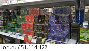 Various Thai balms and ointments in bright packaging. In the center you can see red Tiger Balm boxes, black King Cobra packages, and blue Blue Balm boxes. On the left are green jars of Lanna balm and other brands. These traditional remedies are widely used in Asia to relieve muscle pain, bruises, sprains, colds, and headaches. In the foreground you can see price tags with wholesale and retail offers. On the right in the frame you can see a bottle of Noni Juice, also popular in Thailand as a natural remedy for strengthening the immune system. The photo is perfect for illustrating topics related to Eastern medicine, traditional remedies, healthy lifestyle, and natural products. (2018 год). Редакционное фото, фотограф Анна Кривицкая / Фотобанк Лори