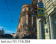 Street scene in St. Petersburg. In the foreground is a red traffic light with a countdown timer, below it are pedestrian crossing signs and a STOP sign. In the background is the facade of a historic building with rich eclectic architectural decor, with stucco and arched windows. A bright sunny day, blue sky, taut power lines and city traffic create the atmosphere of a typical St. Petersburg intersection. People cross the road, cars wait for the traffic light. The photo conveys the atmosphere of life in a big city and combines the architectural heritage of St. Petersburg with a modern street environment. (2019 год). Стоковое фото, фотограф Анна Кривицкая / Фотобанк Лори