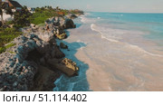 Woman stands on rocky cliff overlooking ocean waves at sunset with Tulum town in Mexico. Стоковое видео, видеограф Ольга Сухарева / Фотобанк Лори