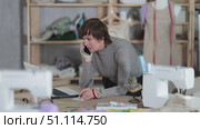 Seamstress talking on phone and working with laptop in sewing workshop. Стоковое видео, видеограф Яков Филимонов / Фотобанк Лори