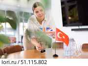 Positive young woman putting flag of Great Britain on the table with flag of Turkey in conference room. Стоковое фото, фотограф Яков Филимонов / Фотобанк Лори