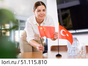 Positive young woman putting flag of China on the table with flag of Turkey in conference room. Стоковое фото, фотограф Яков Филимонов / Фотобанк Лори