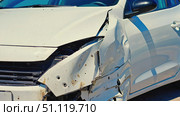 The front edge of a heavily damaged white car: a crumpled fender and a broken bumper, as well as numerous holes and scratches. The damage was probably caused by a collision. Стоковое AI-изображение, AI-художник Светлана  Громак / Фотобанк Лори