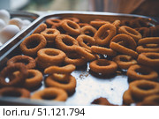 Close-up of crispy golden onion rings piled on a metal tray, creating an enticing display of fried goodness, with blurry boiled eggs visible in the background. Стоковое фото, фотограф Ольга Ильина / Фотобанк Лори