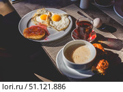 Table is set for a delightful breakfast featuring fried eggs, a pancake with jam, a glass of tea, a bowl of soup, a boiled egg, and a croissant, creating a visually appealing and appetizing scene. Стоковое фото, фотограф Ольга Ильина / Фотобанк Лори