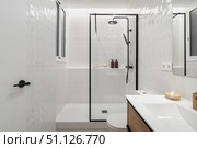 Modern bathroom with a glass shower, white tiles, and wooden accents. Minimalist design featuring a sink and decorative items on the counter. Стоковое фото, фотограф PAv / Фотобанк Лори
