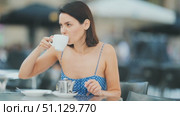 Smiling stylish young brunette woman drinking tea while sitting on terrace of street cafe. Стоковое видео, видеограф Яков Филимонов / Фотобанк Лори