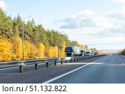 Traffic with trucks with cargo trailers driving on highway transporting goods on autumn day. Cargo Trailer Driving on a Highway. Lorry riding through Industrial Warehouse Area. Copy space. Стоковое фото, фотограф Ирина Михайличенко / Фотобанк Лори