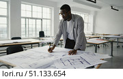 A Focused Architect Analyzing Detailed Blueprints in a Modern Office Setting with Natural Light. Стоковое AI-изображение, AI-художник Владимир Федоров / Фотобанк Лори