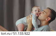 A tender moment between parent and child as the baby is playfully lifted into their arms. A father holds his young son in his arms and kisses him. Стоковое видео, видеограф Воловодов Владимир / Фотобанк Лори