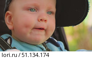Close-up of a smiling baby sitting in a stroller. Baby has cute dimples on his cheeks and two bottom teeth. Happy baby boy wearing an adult baseball cap. Стоковое видео, видеограф Воловодов Владимир / Фотобанк Лори
