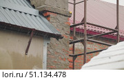 Rain is pouring down against the backdrop of construction. Streams of water run off the roof into the gutter. Unfinished bricks, plaster and metal roofing against scaffolding. Slow motion of rain. Стоковое видео, видеограф Воловодов Владимир / Фотобанк Лори