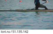 A man paddles a canoe on calm blue waters, displaying muscular legs and a focused pose. Sunlight reflects off the surface. Close-up of an athlete in a canoe during training. Стоковое видео, видеограф Воловодов Владимир / Фотобанк Лори