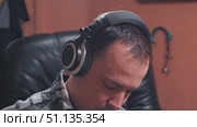 A man wearing large headphones sat comfortably in a leather chair, dressed in a plaid shirt, immersed in the soundtrack in a cozy setting. Close-up. Стоковое видео, видеограф Воловодов Владимир / Фотобанк Лори