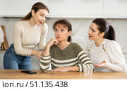 Sad woman sits silently in kitchen, adult girls sympathize and comfort her. Стоковое фото, фотограф Яков Филимонов / Фотобанк Лори