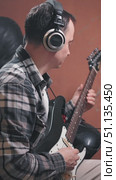 A man wearing headphones, wearing a plaid shirt and a white T-shirt, is playing an electric guitar solo. The guitarist works at a recording studio. Стоковое видео, видеограф Воловодов Владимир / Фотобанк Лори