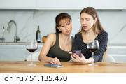 Two sad middle-aged women looking at the phone display while sitting at the table at home. Стоковое фото, фотограф Яков Филимонов / Фотобанк Лори