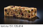 Nutrient dense cereal bar spinning with mixed nuts, seeds, dried fruit on sleek reflective black surface, showcasing wholesome ingredients against crisp white backdrop. Стоковое AI-видео, аниматор Юрий Поздников / Фотобанк Лори