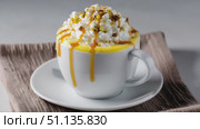 Creamy pistachio latte macchiato garnishing whipped cream, caramel drizzle, chopped nuts, sitting in white ceramic cup atop saucer, resting on brown textured napkin. Стоковое AI-видео, аниматор Юрий Поздников / Фотобанк Лори