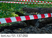 Заграждение в виде полосатой красно-белой оградительной ленты вокруг ямы, раскопанного газона. обеспечение безопасности на месте ремонтных работ в парке. Стоковое фото, фотограф Нина Чалых / Фотобанк Лори