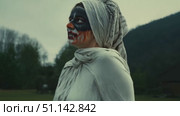 A woman dressed in haunting garments and striking face paint walks through a darkened forest landscape. Стоковое AI-видео, аниматор Данила Большаков / Фотобанк Лори