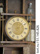 Vintage table clock with Roman numerals on the dial. The case is made in a classic style with metal decorative elements - twisted golden posts and wooden inserts. The clock shows the time around 12:08. The dial has a beige-gold hue, the hands are made in an elegant style typical of retro models. In the background, old bottles and wooden shelves are visible, which enhances the atmosphere of antiquity and coziness. The photo conveys a sense of time, nostalgia and vintage interior, suitable for illustrations of topics related to history, retro decor and antiques. Стоковое фото, фотограф Анна Кривицкая / Фотобанк Лори